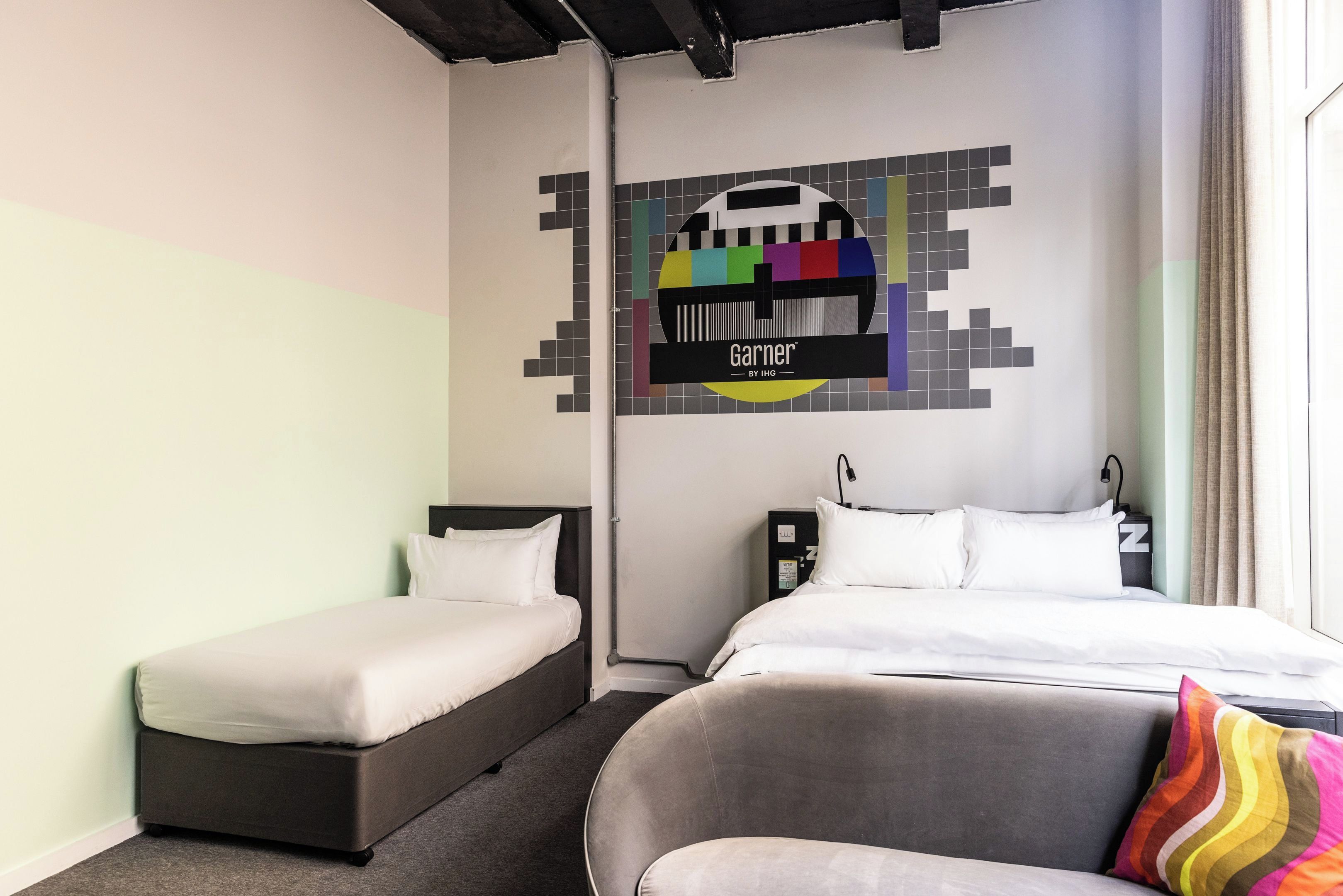 A hotel room with two single beds, a grey sofa, and a colorful wall art piece.