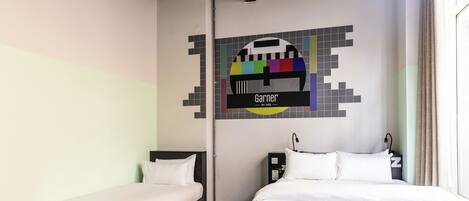 Een hotelkamer met twee eenpersoonsbedden, een grijze bank en een kleurrijk kunstwerk aan de muur.