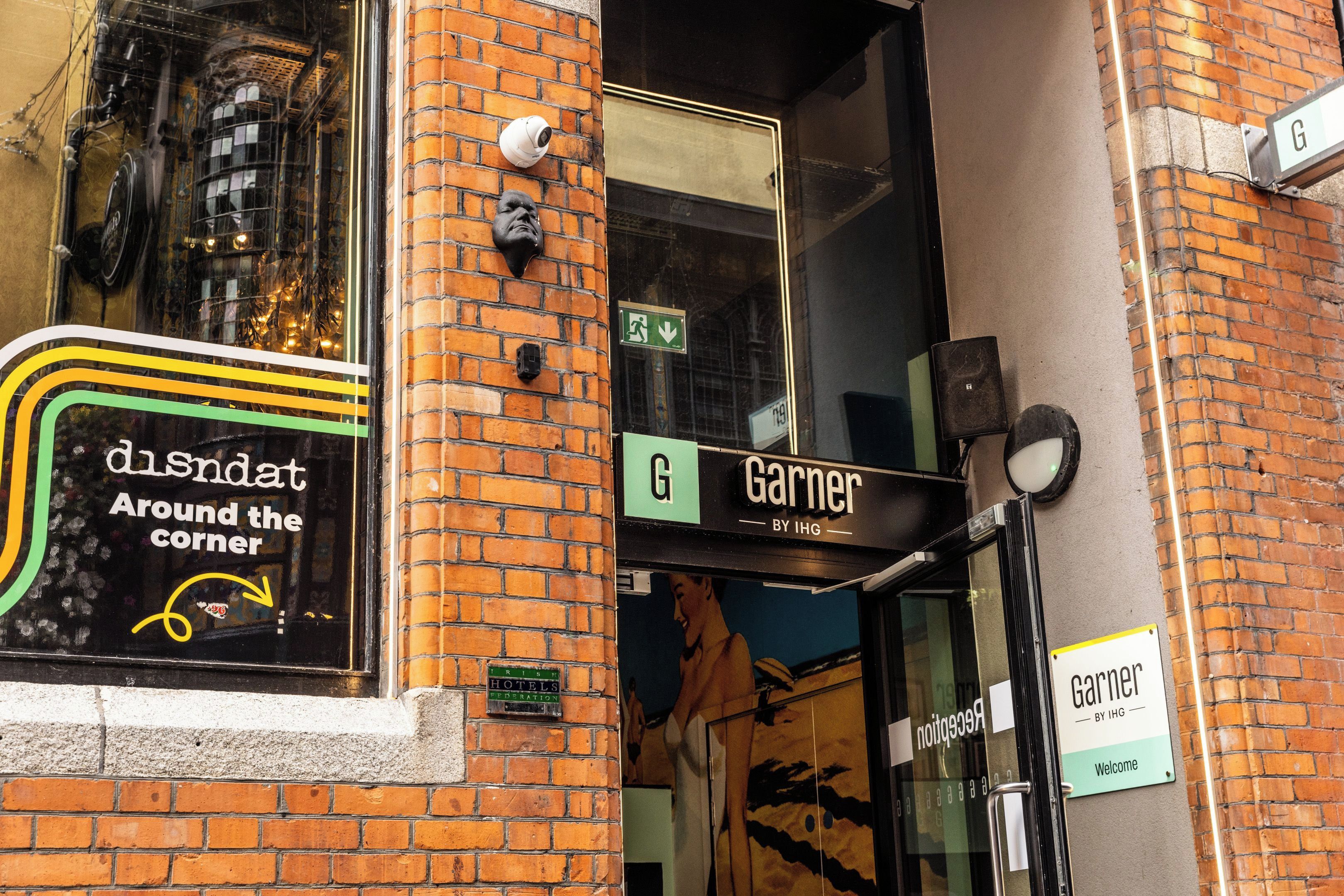 L’entrée d’un hôtel, avec une enseigne indiquant « Garner » et une publicité visible dans la vitrine pour « dIsNat, tout près d’ici ».