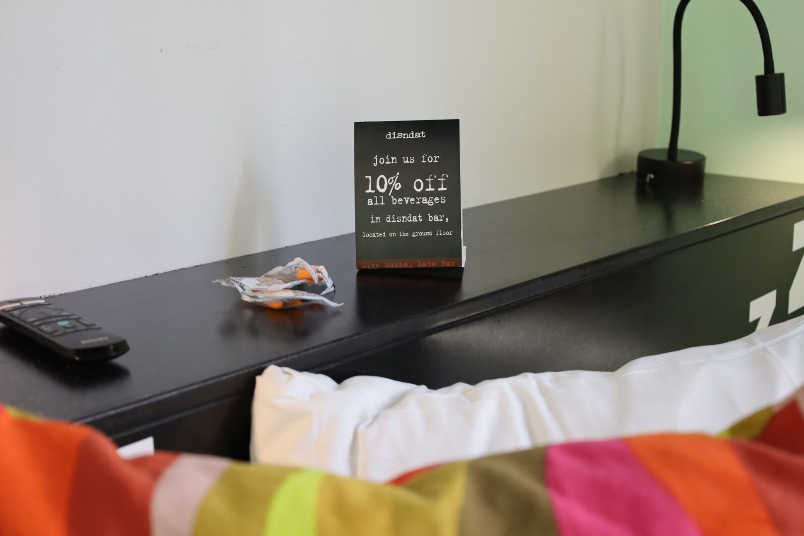 A hotel room with a sign offering a 10% discount on beverages, a remote control, and a neatly made bed.