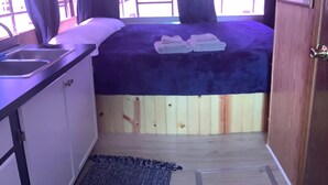 Ein gemütlicher Raum mit Bett, einer kleinen Küchenzeile und einem Fenster mit Vorhängen.