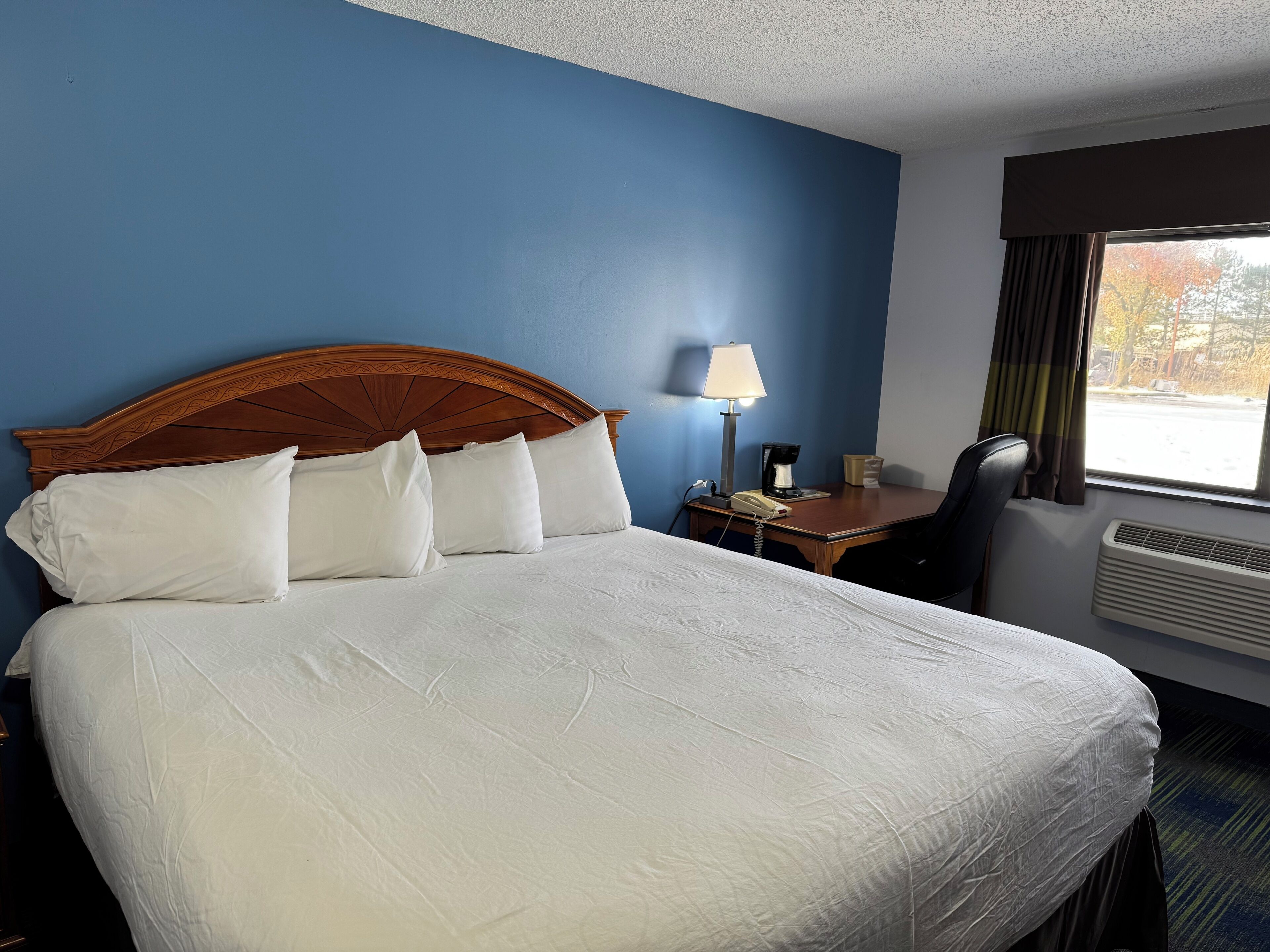 A hotel room with a large bed, a desk with a lamp, a chair, and a window with curtains.