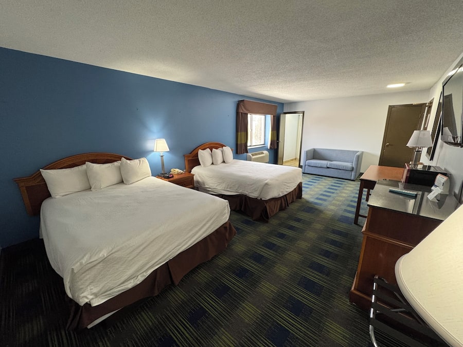 A hotel room with two beds, a desk, a chair, a mirror, and a window with curtains.