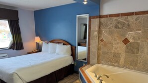 A hotel room with a bed, a large mirror, a bathroom with a bathtub, and a window with curtains.