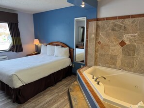 A hotel room with a bed, a large mirror, a bathroom with a bathtub, and a window with curtains.