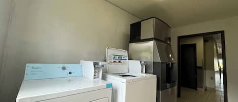 Uma área de lavanderia com máquina de lavar e secadora Whirlpool, uma geladeira de aço inoxidável e um armário branco.