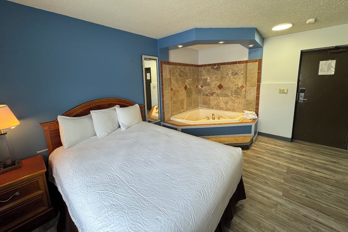 A hotel room with a large bed, a bathroom with a bathtub, and a door.
