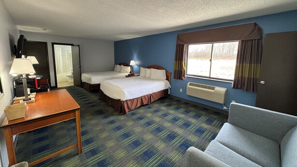 A hotel room with two beds, a desk, a chair, a TV, and a window with curtains.
