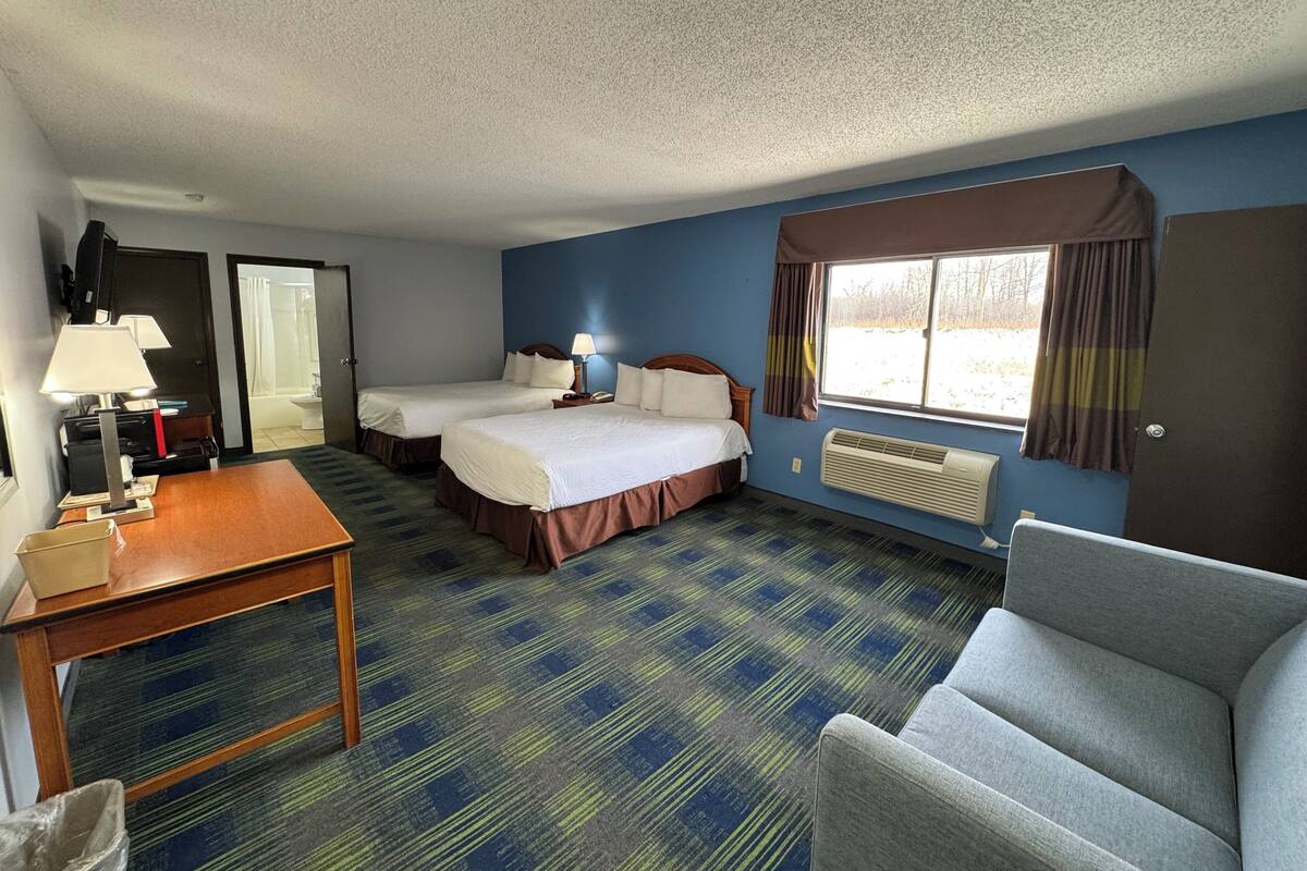 A hotel room with two beds, a desk, a chair, a TV, and a window with curtains.
