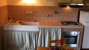 Cocina compacta con lavamanos, estufa, horno y un pequeño comedor con mesa y silla.