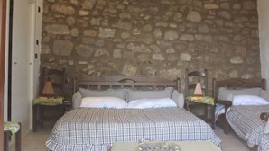 Una habitación con pared de piedra, dos camas con ropa de cama a cuadros, cabeceros de madera y una mesita con bandeja.