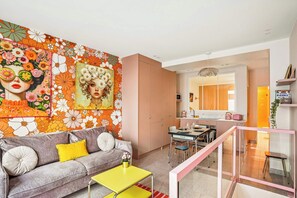 A modern living room with a vibrant floral wall mural, a grey sofa with yellow cushions, a yellow coffee table, and a dining area with a glass railing.