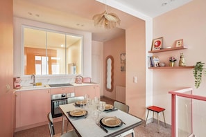 A modern kitchen with pink cabinets, a dining table set for four, and a large mirror above the sink.