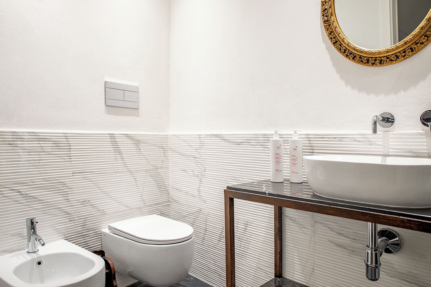 A modern bathroom with a white sink, a toilet, and a mirror with an ornate gold frame.