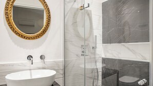 A bathroom with a white sink, a gold-framed mirror, a glass shower enclosure, and a marble-tiled shower area.