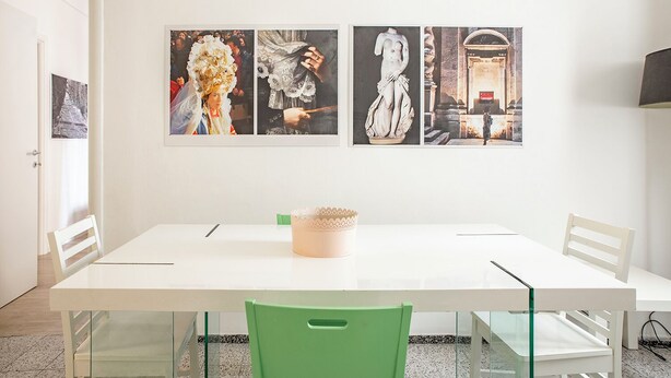 A dining area with a white table, green chairs, and three framed artworks on the wall.