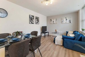 A modern living room with a dining area, a flat-screen TV, and abstract wall art.