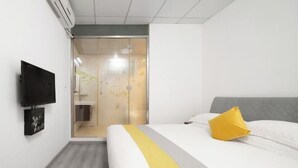 Ein Hotelzimmer mit Bett, einem an der Wand befestigten Fernseher und einem Duschbereich hinter einer Glastür.