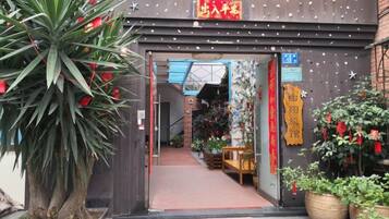 An entrance to a building with a red sign, a pathway leading inside, and potted plants outside.