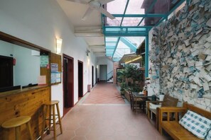 Corredor com balcão de atendimento de madeira, parede coberta de recados e escada para um andar superior.