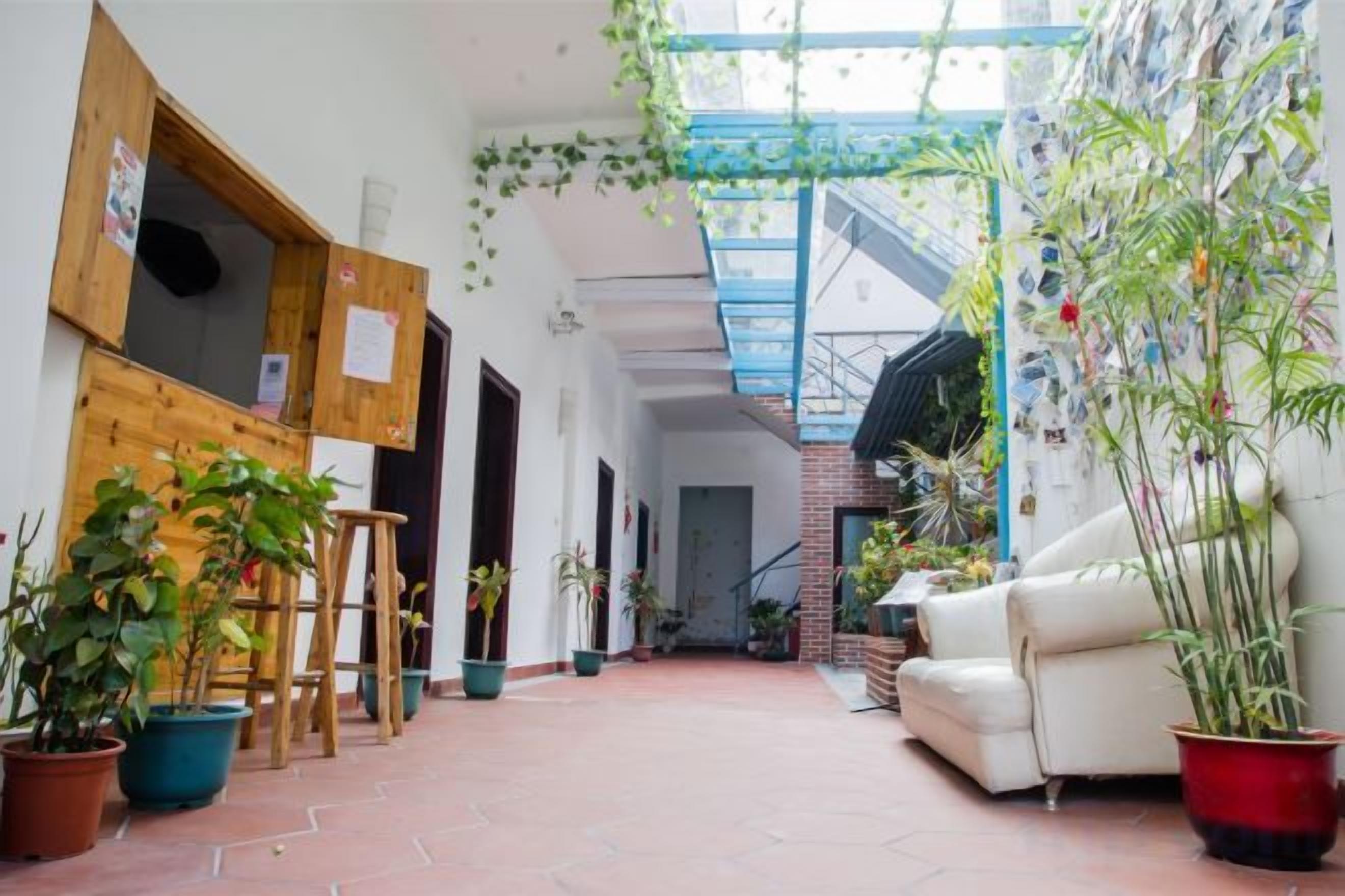 A narrow indoor corridor with a staircase, wooden doors, and potted plants.