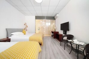Ett hotellrum med två sängar, ett skrivbord, en stol, en TV och en glasdörr som leder till ett badrum.