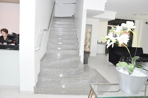 Una escalera que lleva al segundo piso, una zona de recepción con mostrador y una orquídea en maceta.
