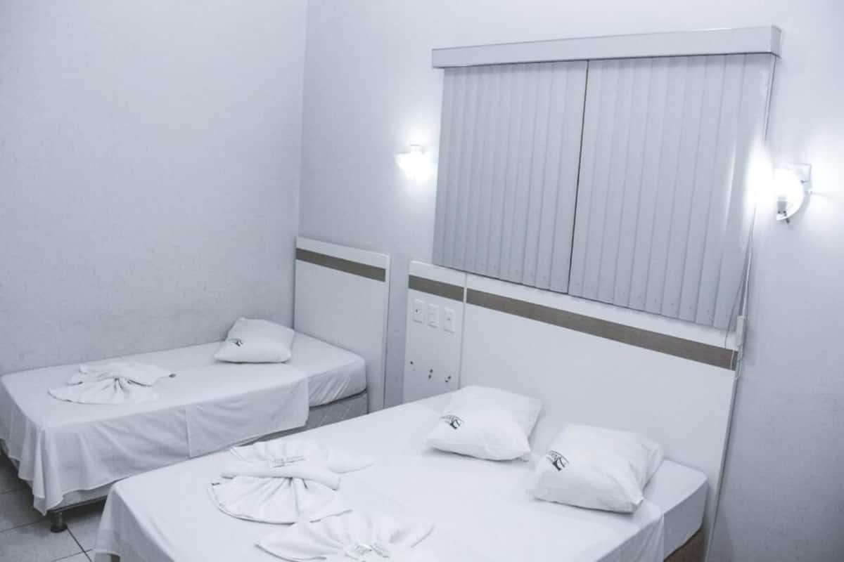 A room with two single beds, each with a pillow and a neatly folded white shirt on the bed.