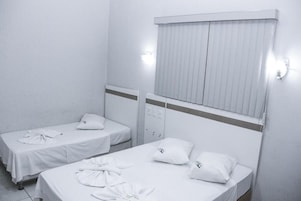 Una habitación con dos camas individuales, cada una con una almohada y una camisa blanca doblada con cuidado sobre la cama.