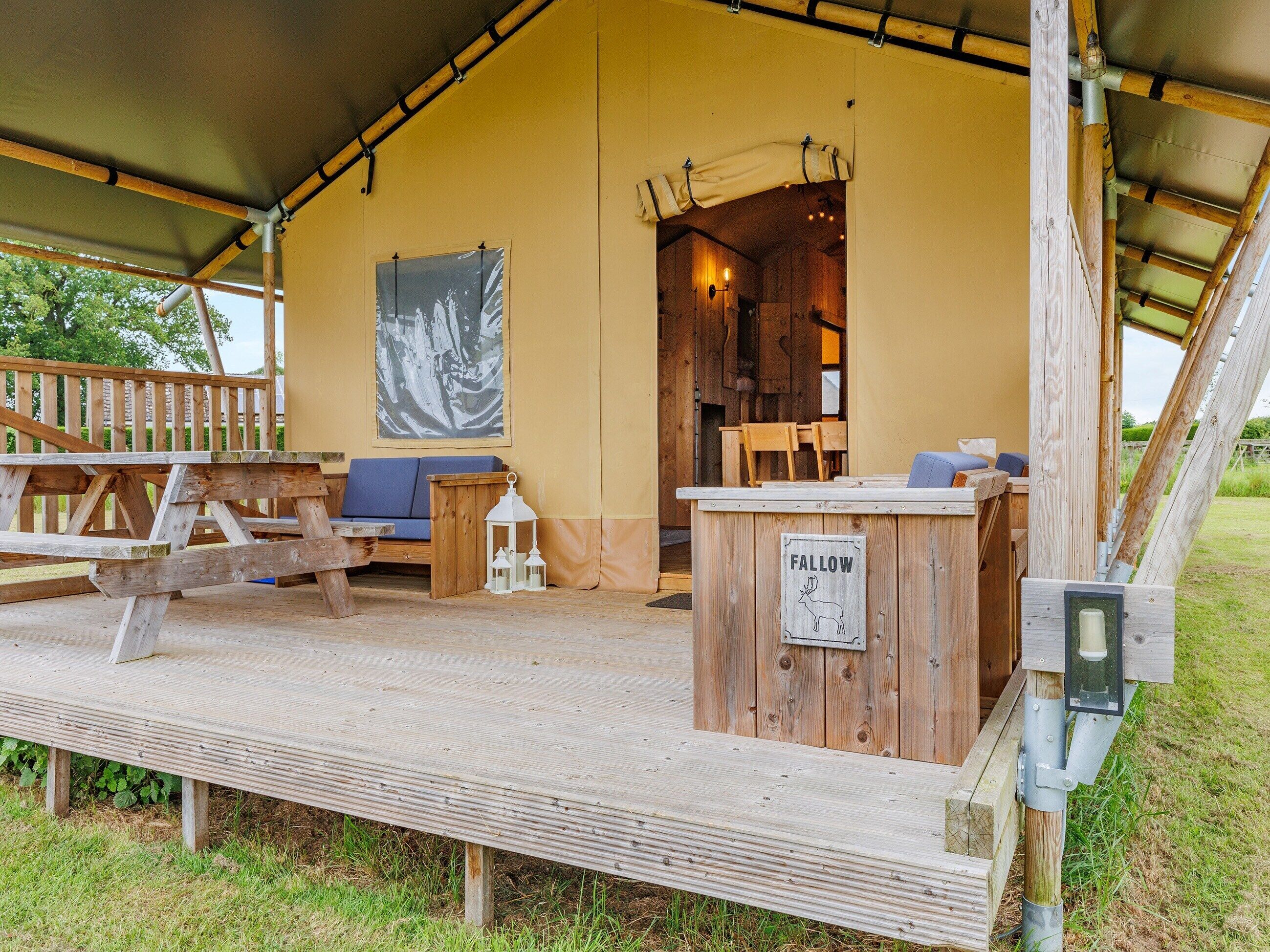 A rustic wooden cabin with a covered porch, a seating area with a blue sofa, and a sign indicating a fallow area.
