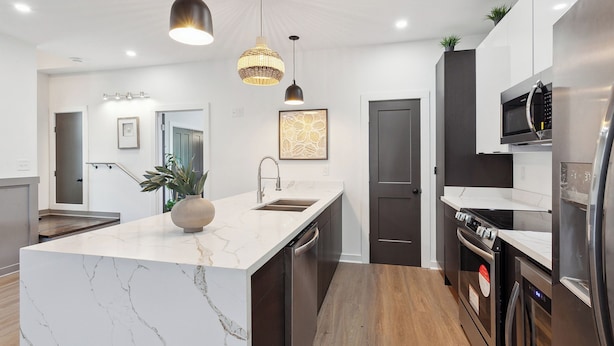 A modern kitchen with a marble island, stainless steel appliances, pendant lighting, and a dark door.