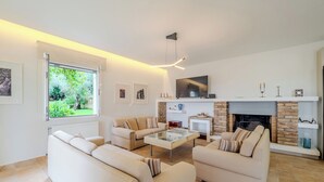 Ein modernes Wohnzimmer mit Kamin, Fernseher und großem Fenster mit Blick auf einen Garten.
