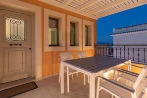 An outdoor patio with a table and chairs, a door with decorative glass, and a view of the sea at dusk.