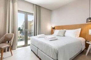 A modern hotel room with a large bed, a chair, and a view through a sliding door.