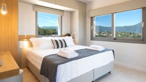 A modern bedroom with a large bed, two bedside tables, a window with a view of the outdoors, and a wooden panel wall.