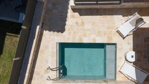 Vista aérea de una piscina con solárium de piedra, rodeada de sillones de descanso y una pequeña zona de terraza.