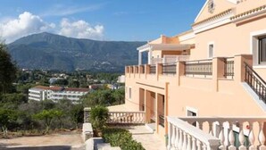Un edificio de dos pisos con balcones, un sendero de piedra y montañas al fondo.