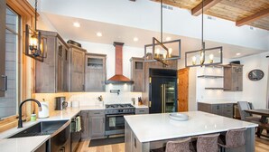 A modern kitchen with wooden cabinets, a central island with bar stools, a stainless steel refrigerator, and pendant lighting. - Luxurious Downtown Penthouse w/ Hot Tub! (Whitefish)