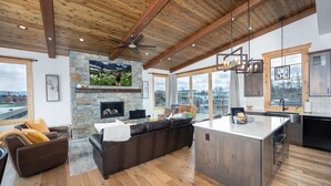 A spacious living area with a stone fireplace, a large leather sofa, and a wooden ceiling. - Luxurious Downtown Penthouse w/ Hot Tub! (Whitefish)