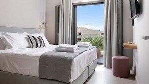A modern bedroom with a large bed, a flat-screen TV mounted on the wall, and a window with curtains. - Onore Sunset Suite & pool | Dasia (Dassia)