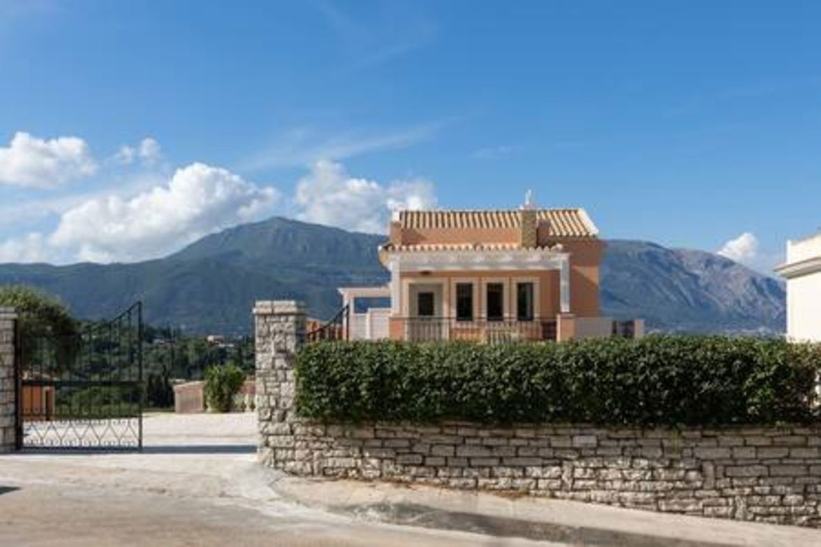 A building with a stone wall and a gate, set against a mountainous backdrop.