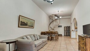 A living room with a sofa, dining table, chairs, a TV, a staircase, and a kitchen area. - Villa Delphine by Tsiolis family ★ shared pool (Katavolos)
