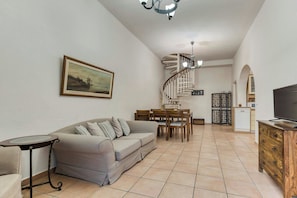A living room with a sofa, dining table, chairs, a TV, a staircase, and a kitchen area.