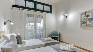 A hotel room with two beds, a chair, a window with curtains, a wall-mounted lamp, and a framed picture. - Villa Delphine by Tsiolis family ★ shared pool (Katavolos)