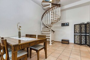 A dining area with a wooden table, chairs, a vase, a spiral staircase, and a decorative screen.