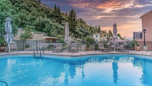 A swimming pool with lounge chairs and umbrellas, surrounded by stone walls and trees. - Villa Delphine by Tsiolis family ★ shared pool (Katavolos)