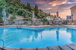 A swimming pool with lounge chairs and umbrellas, surrounded by stone walls and trees.