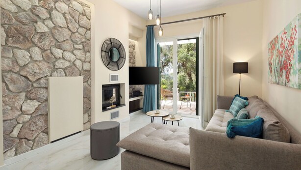 A modern living room with a stone wall, a flat-screen TV, a sofa, and a dining area with a table and chairs. - Achileio Alexandros Cottage (Gastouri)