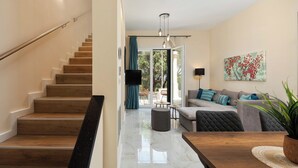 A modern interior with a wooden staircase, a living area with a sofa and a coffee table, and a dining area with a wooden table. - Achileio Alexandros Cottage (Gastouri)