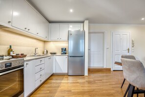 Une cuisine moderne avec des armoires blanches, un réfrigérateur en acier inoxydable et un plancher en bois.